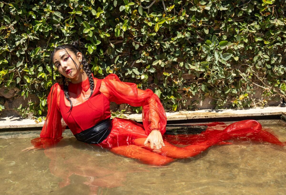 Striking portrait of a woman in a red dress lounging elegantly by a garden pool.