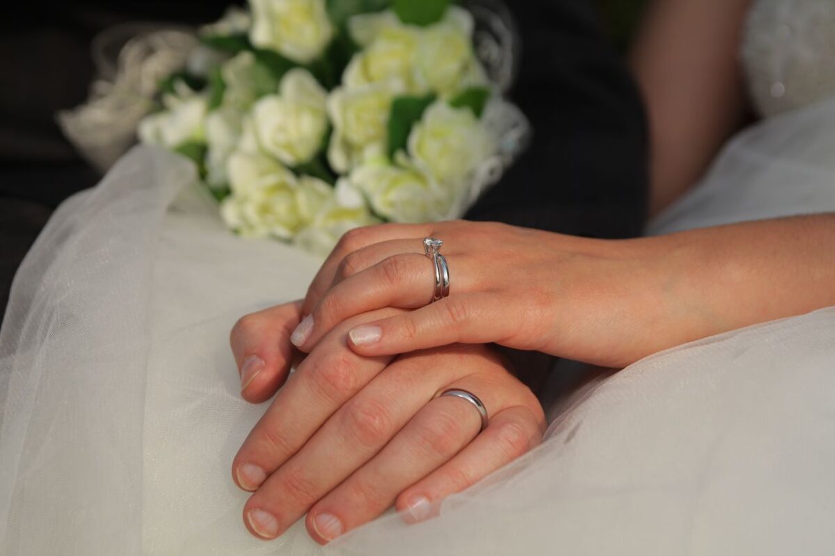 Close-up of newlywed hands with wedding rings and a bouquet of white roses.