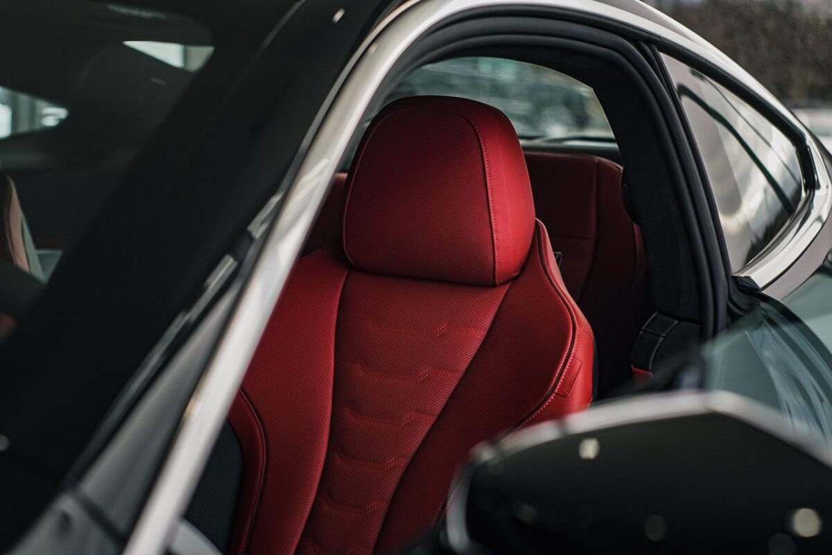 A close-up shot of a sleek car interior featuring a luxurious red leather seat illuminated by soft sunlight.
